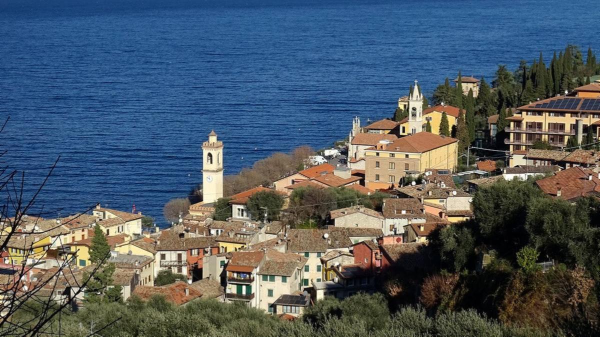 Castelletto di Brenzone am Gardasee, Häuser und zwei Glockentürme direkt am Ufer, dahinter das steile Westufer