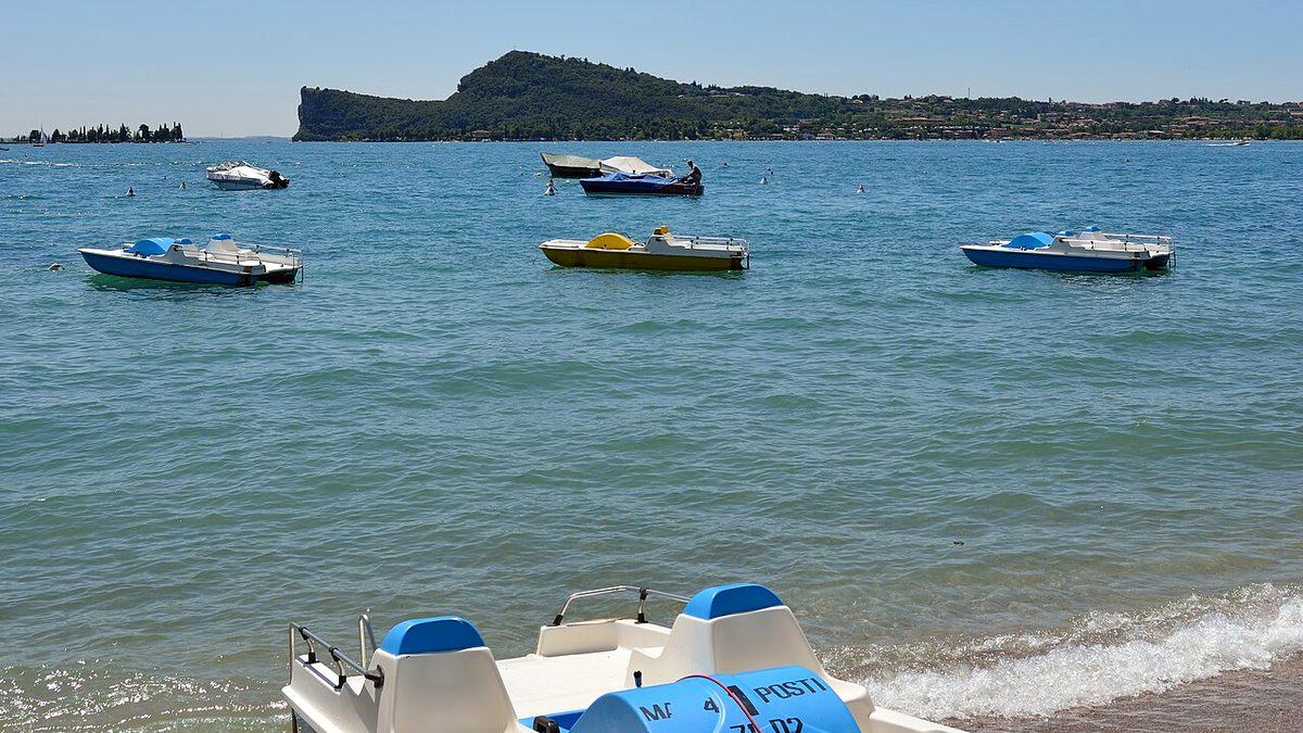 Tretboote auf dem Wasser bei San Felice del Benaco am Gardasee, dahinter eine bewaldete Landzunge