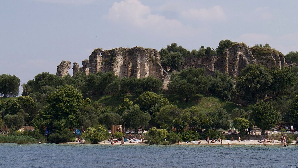 Jamaica Strand an der Landzunge von Sirmione mit flachem Wasser, dahinter Olivenbäume und die Grotte di Catullo