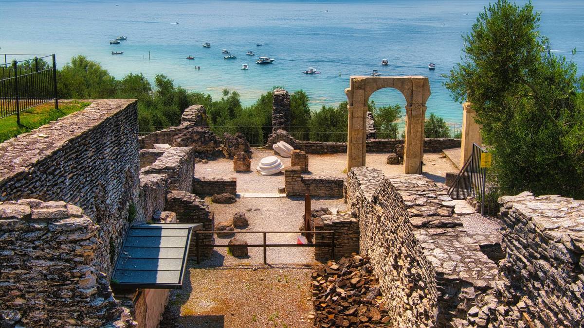 Ausgrabung der Grotten des Catull über dem türkisfarbenen Wasser des Gardasees, dahinter ankernde Boote