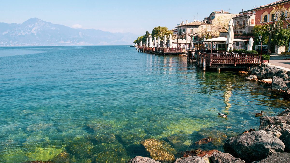 Uferpromenade von Gardone Riviera mit klarem Wasser und Bergen