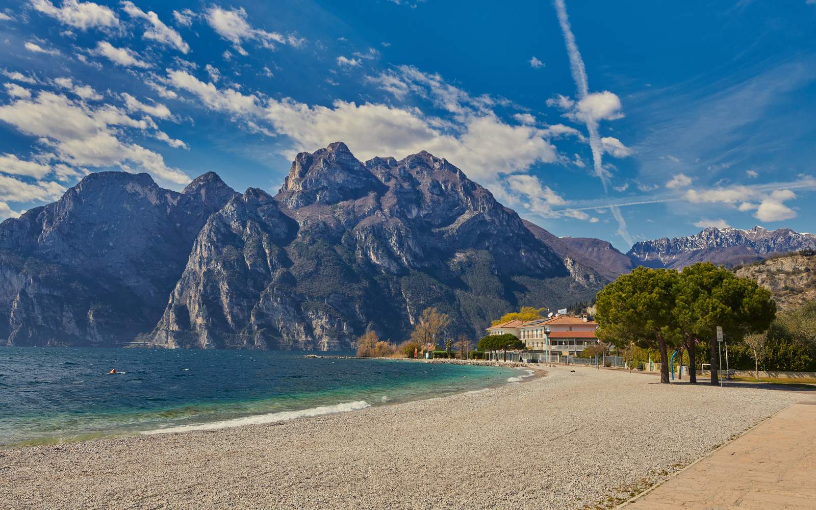 Breiter Kiesstrand am Gardasee mit türkisem Wasser und Felswänden dahinter