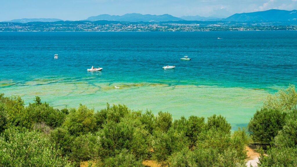 Smaragdgrünes flaches Wasser am Jamaika Strand bei Sirmione mit Booten