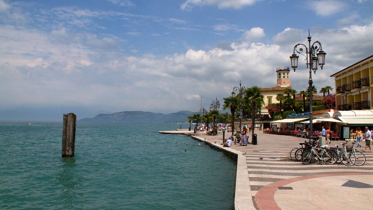 Gepflasterte Uferpromenade von Lazise am Gardasee mit Palmen, Laternen und Blick über das Wasser