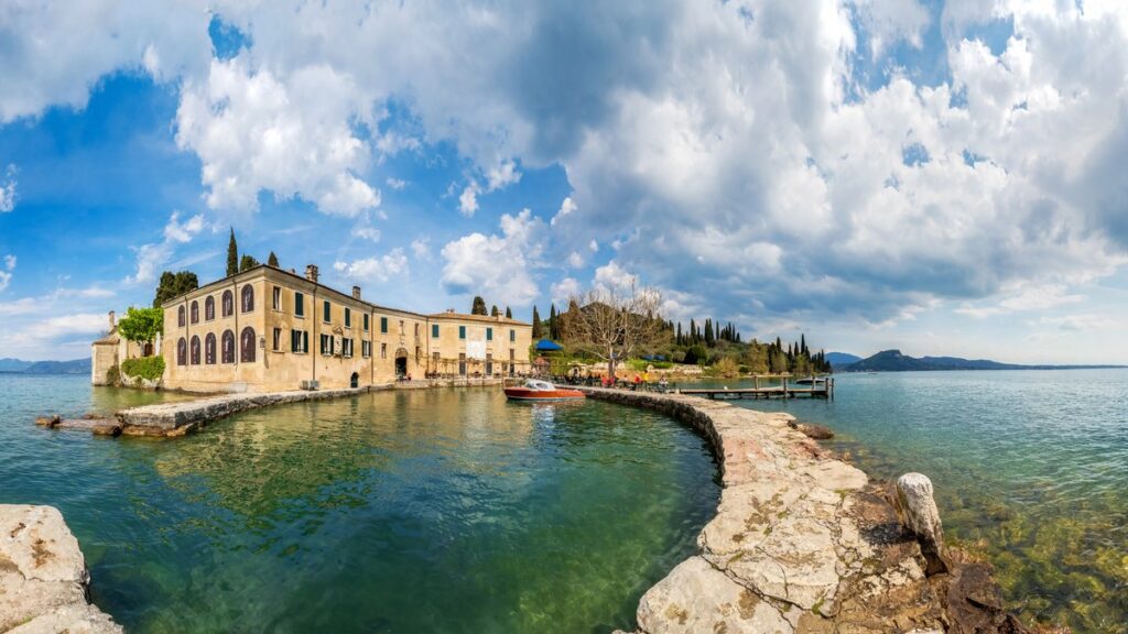 Der geschwungene Steinsteg und die Locanda von Punta San Vigilio, dahinter der Gardasee