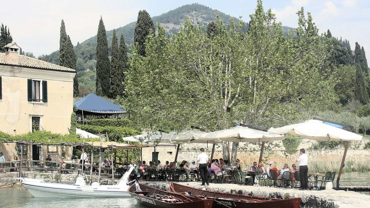 Restaurant der Locanda San Vigilio am Ufer mit Sonnenschirmen und hölzernen Ruderbooten