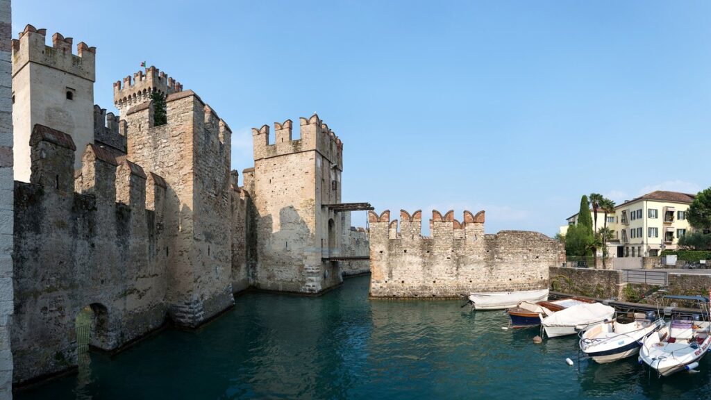Mauern und Türme der Rocca Scaligera in Sirmione am Wassergraben, davor Boote im Hafenbecken