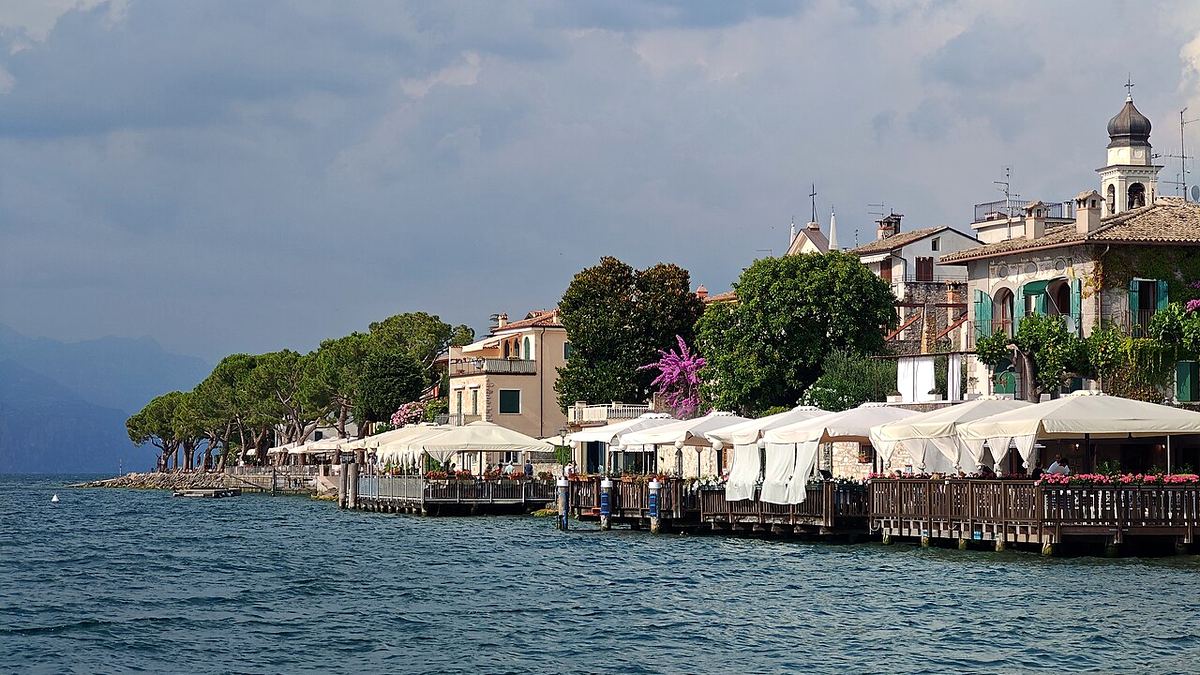 Seepromenade von Torri del Benaco mit Restaurantterrassen über dem Wasser und Pinien am Ufer